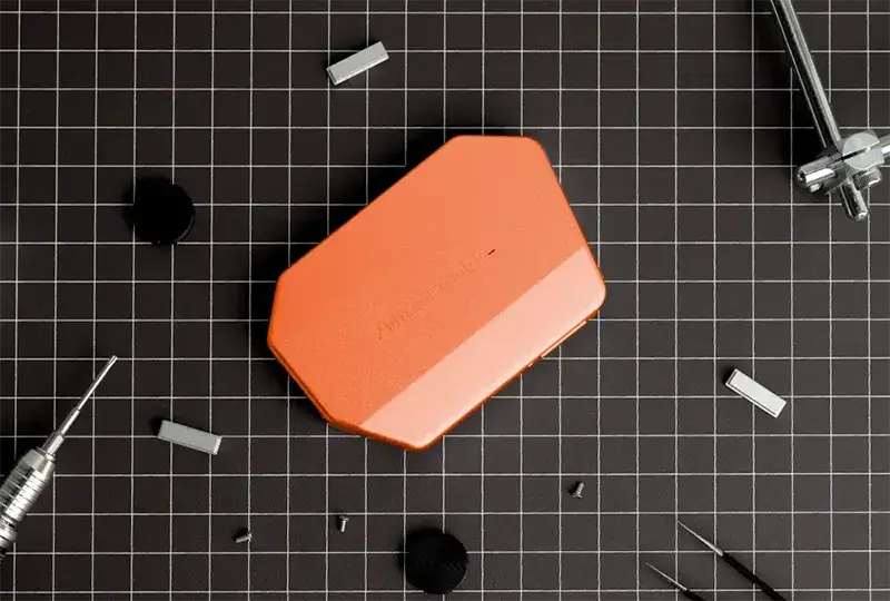 Orange WhisPrompt prototype resting on a gridded workbench